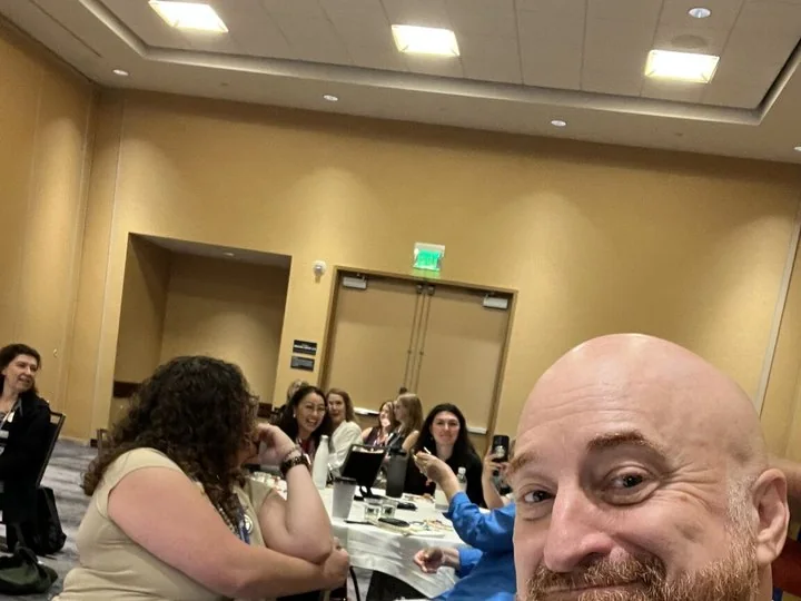 Chris Gloede taking a selfie with state society leaders seated at tables behind him.