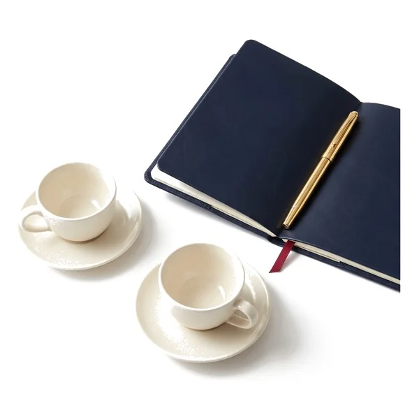 Two coffee cups beside an open notebook.