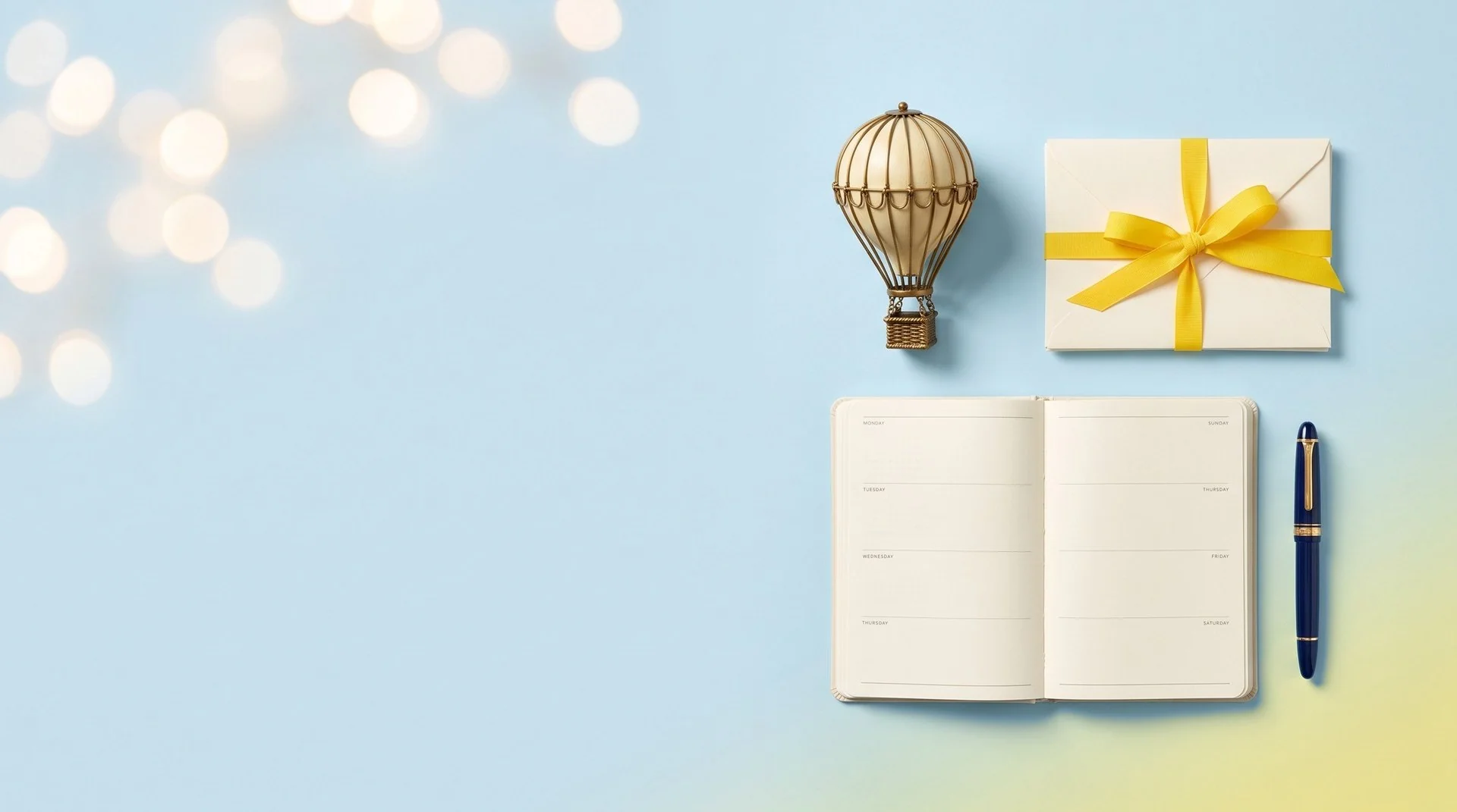 A brass hot air balloon model, cream envelopes tied with yellow ribbon, an open week planner and a navy fountain pen on a pale blue backdrop fading to light yellow in the corner.