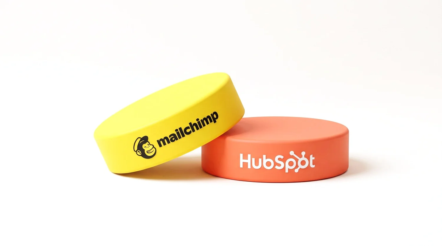 A yellow puck with the Mailchimp logo resting partly on top of a coral puck with the HubSpot logo.