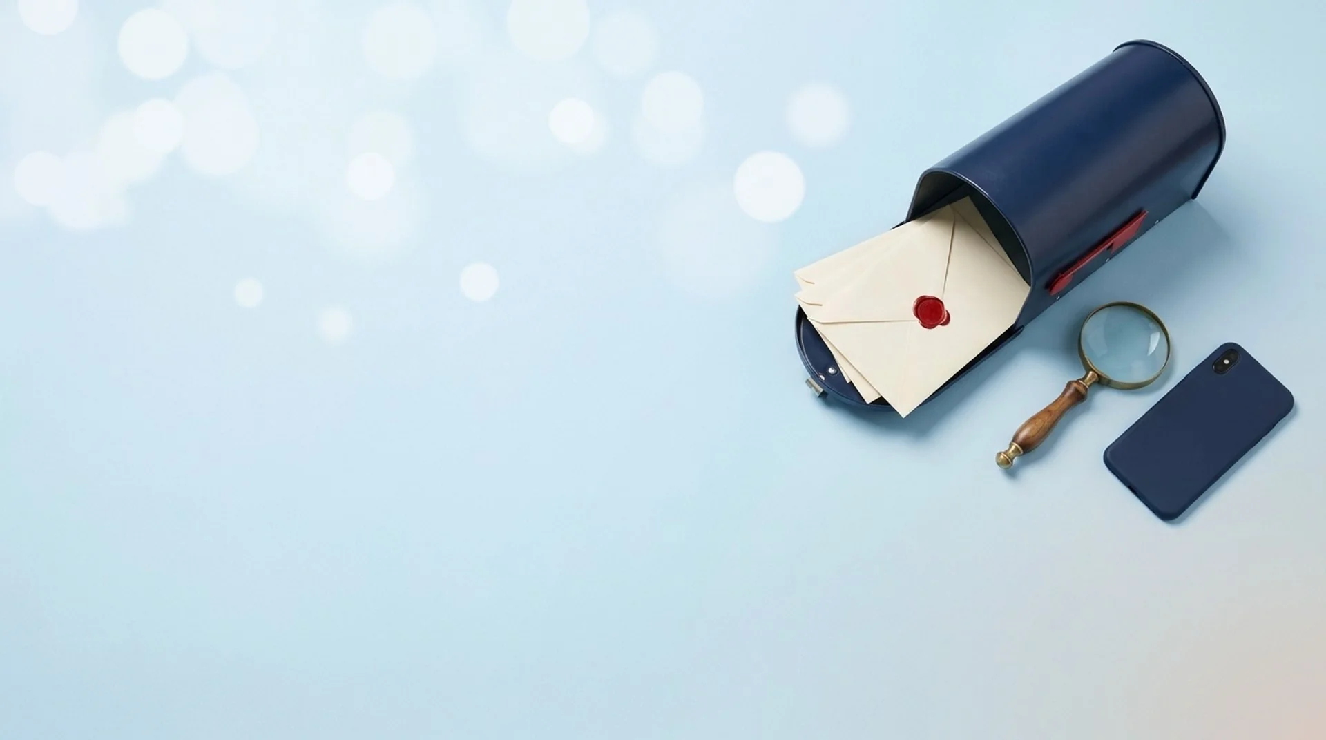 A navy mailbox lying open with cream envelopes sliding out, beside a brass magnifying glass and a phone.